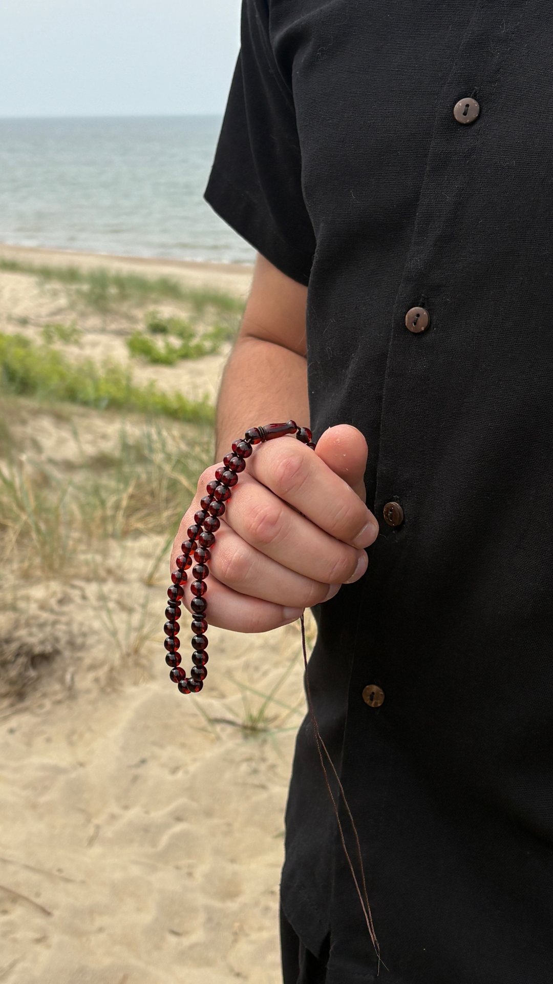 Deep cherry amber tasbih held close, intimate detail